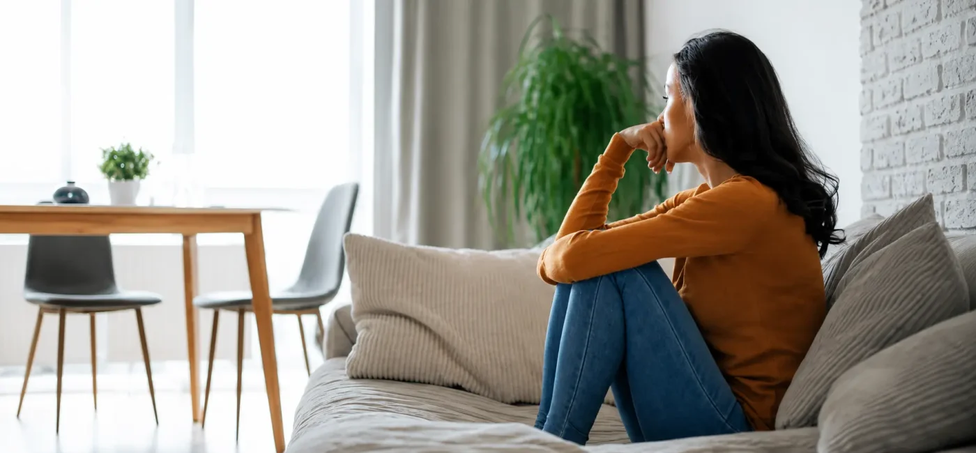 Woman sitting alone on a sofa looking thoughtful, highlighting the importance of mental and emotional health during weight loss, stress management, emotional well-being, and sustainable healthy lifestyle habits.